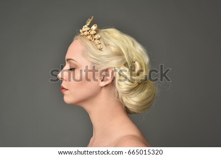 portrait of a blonde woman wearing a tiara, grey background.