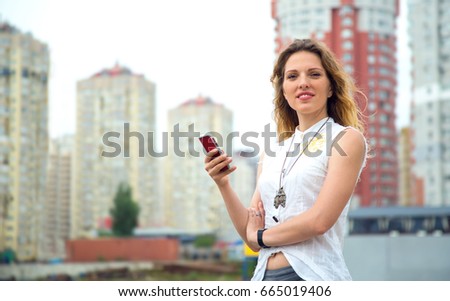 Woman is holding a mobile phone standing in the background of a city street. 30 year old woman.