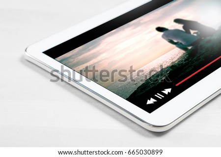 Online movie stream with mobile device. Close up to white tablet on wooden table with imaginary video player and film streaming service.