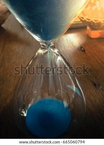 Blue sand running countdowns in hourglass on wooden top vintage color background