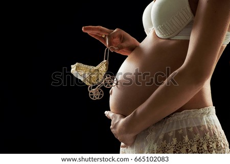 Pregnant girl with a toy carriage on her tummy on a black background