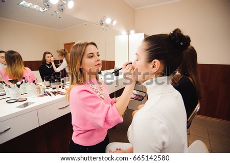 Professional make-up artists work with beautiful young women. School of professional make-up