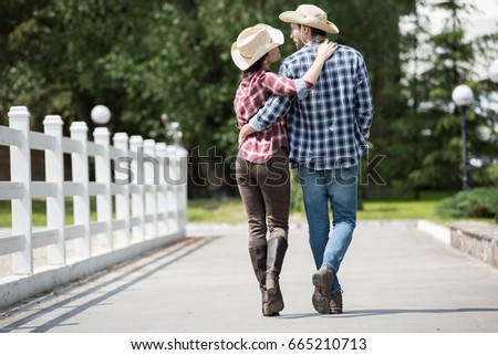 back view of cowboy with his girlfriend walking on pathway in park at daytime