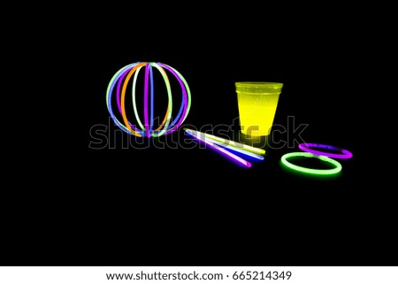 Yellow fluorescent glass and ball with glow sticks neon light on back background. variation of different colored chem lights