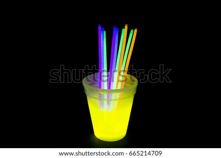 Yellow fluorescent glass with glow sticks neon light on back background. variation of different colored chem lights