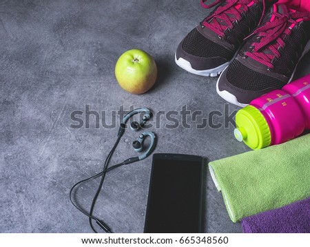 Fitness equipment: sport shoes, bottle of water, smartphone with headphones, an apple and  a towel on grey background