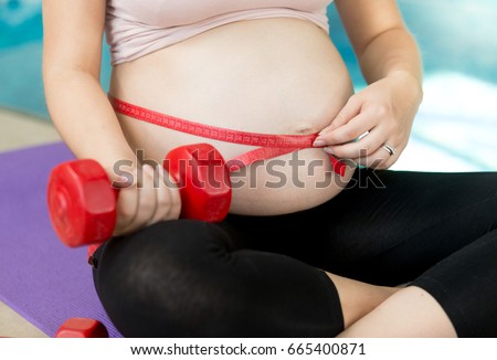 Young pregnant woman doing fitness and measuring belly with measuring tape