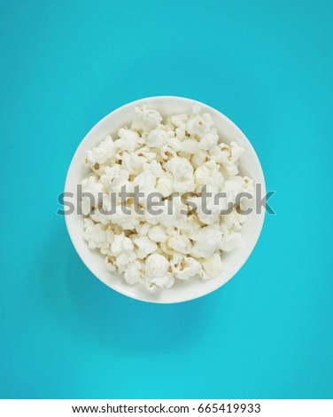 White fluffy movie theater popcorn in a bowl on blue background, top view. Cinema concept with classical popcorn