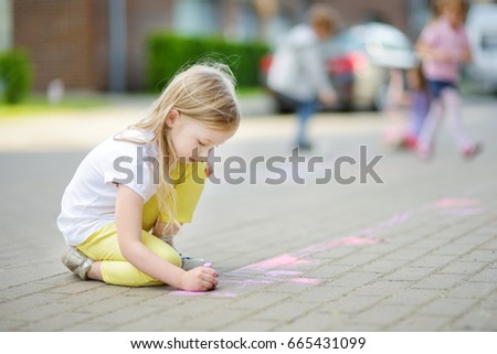 Cute little girl drawing with colorful chalks on a sidewalk. Summer activity for small kids. Creative leisure for family. 