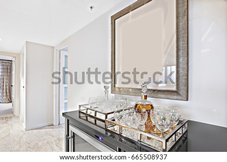 Wine glasses and cups on the tray with bottle  on the black cupboard near to the wall and in the middle of the house with white walls