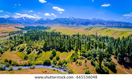Kazakhstan. Summer landscape. A beautiful view of the foothill area against the background of green trees, clouds and snowy peaks. Nature and travel. Aerial view.  Royalty-Free Stock Photo #665536048