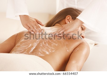 Masseur applying massage cream on young woman's back.?