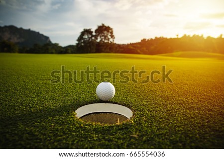 selective focus. white golf ball near hole on green grass good for background with sunlight and lens flare effect