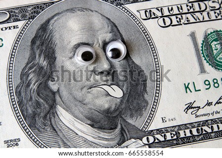 Franklin with big eyes showing tongue on the banknote 100 dollars. Financial concept.