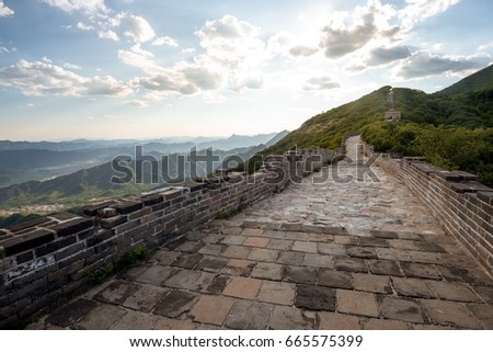 Rural part of the Great Wall of China that stretches throughout the mountains, in slight disrepair, shot in a sunny weather with blue sky and scant clouds