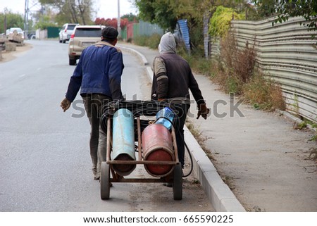 Two workers roll a cart with gas bottles