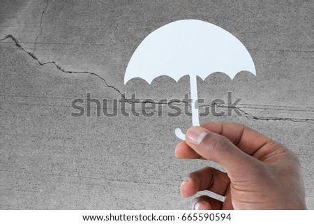 hand holding an umbrella in paper against concrete wall with crack