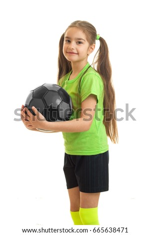 vertical portrait of cutie little girl in green shirt holding a soccer ball in hands