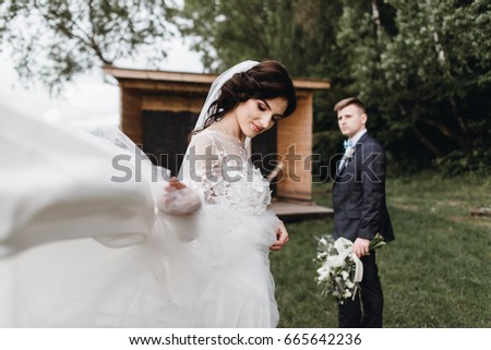 The newlyweds are walking near a wooden house by the lake. Tenderness and the atmosphere is calm. Beautiful bouquet and dress waving in the wind