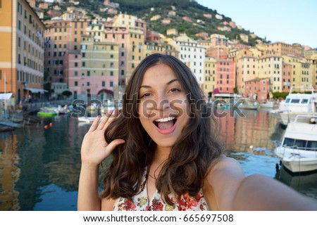 Happy young woman tanned taking selfie photo in a typical italian landscape with harbour and colorful houses for italian holidays in Liguria, Italy