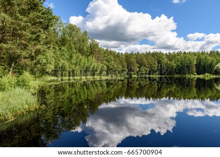 White clouds on the blue sky over forest lake with reflections