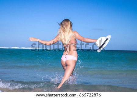 Young blonde woman with hat and in swimsuit is coming into the ocean of tropical Bali island, Indonesia.