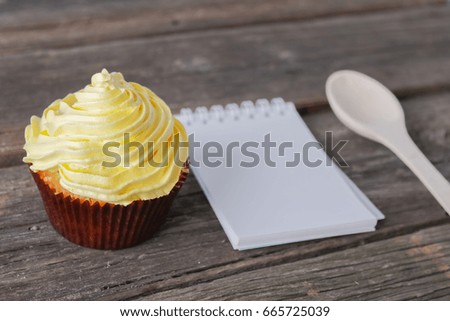 Capcake on a wooden background with a blank notebook