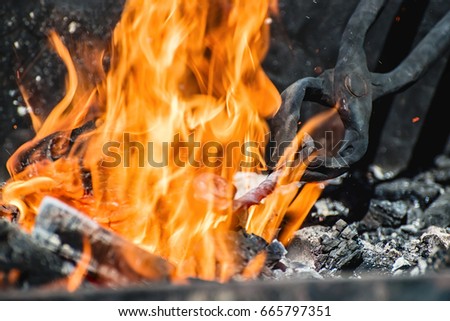 tongs holding a metal workpiece in hot coals