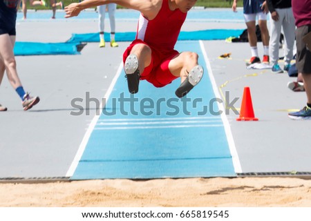 A high school male long jumper and triple jumper in the air with his legs parallel to the sand getting ready to land during a competition Royalty-Free Stock Photo #665819545