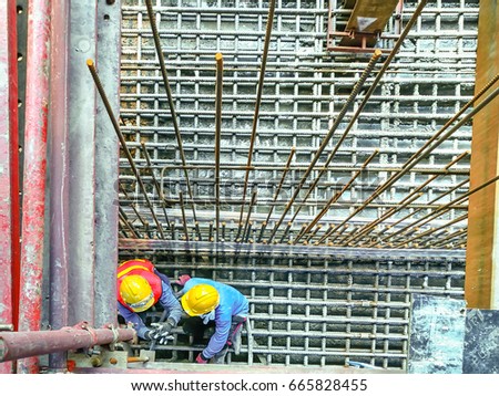 Construction workers sit on steel with concrete foundation and check the quality of round bar.(top view image)