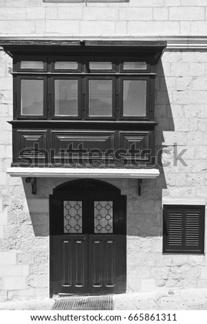 Building with traditional colorful maltese balcony and door in historical part of Valletta. Black and white picture