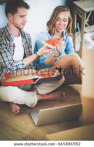 Young couple have a pizza lunch break on the floor after moving into a new home with boxes around them