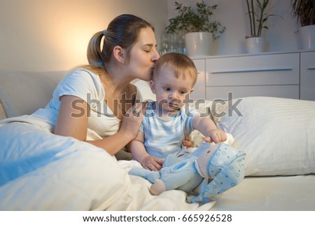 Portrait of young mother kissing her baby boy before going to sleep at night