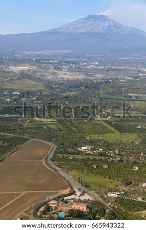 Aerial photography of fields and farmhouses, with volcano Etna casting smoke, on the horizon, island of Sicily, Italy