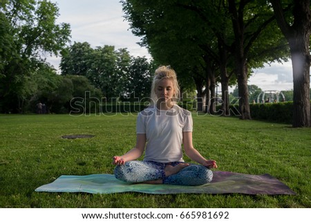 young happy beautiful barefoot blonde girl in bright clothing doing yoga in city Park. Lotus pose