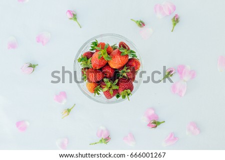 Glass bowl with fresh plucked strawberries and petals of English roses and small buds.