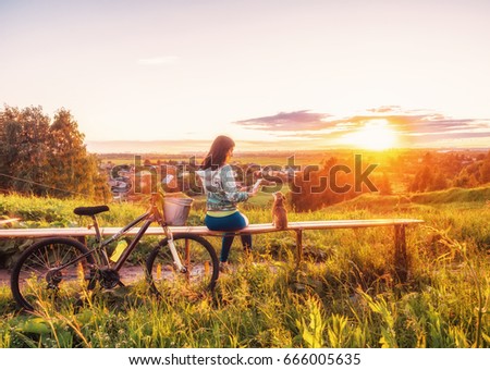 Girl and a dog are looking at a beautiful sunset on the horizon. Walking with a dog on a bike in the evening. Young girl and a dwarf chihuahua look at the setting sun in the evening. People at sunset