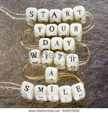 inscription start your day with a smile made from wooden toy blocks stringed on a rope and laying on the shining foil background.