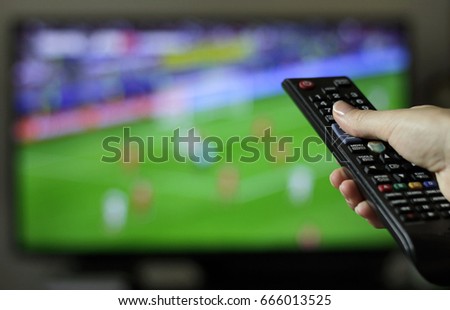 Female tuning into football or soccer game holding a remote control Royalty-Free Stock Photo #666013525