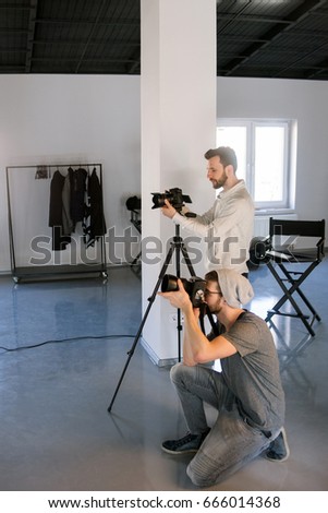 Two photographers taking shots in studio. Professional photo and video production team work together. Fashion photo session backstage