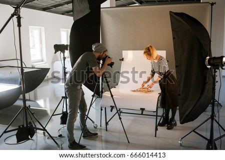 Creative team shooting commercials. Back view of photographer taking object shots with assistant in studio interior. photoshoot backstage
