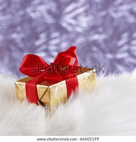 Golden gift box with red ribbon on white fur against blue blurred background