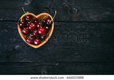 Cherries in a wooden bowl in a heart shape. Natural wooden burnt table. Fresh food concept. Fruit. Summer time