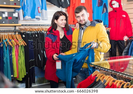 Positive couple deciding on track jacket in sports clothes store