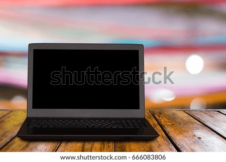 the notebook computer is on the wooden table and blurred image of the party ribbon with beautiful bokeh from the lights as background