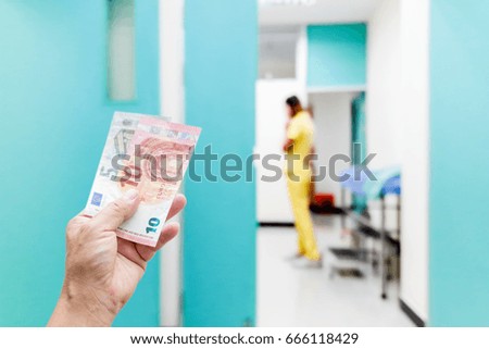 Man hold cash, blurry picture of a nurse assistant walking in the doctor's office as background, she is very busy.