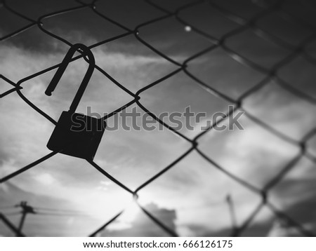 Steel wire net fence with unlocked padlock on blurred sky background. Concept unlocked life and dream.Black and white picture