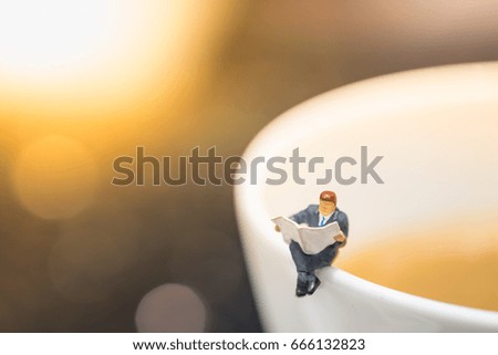 Reading, relaxing, hobby concept. Close up of businessman miniature mini figures sitting and read a newspaper on the cup of hot coffee.
