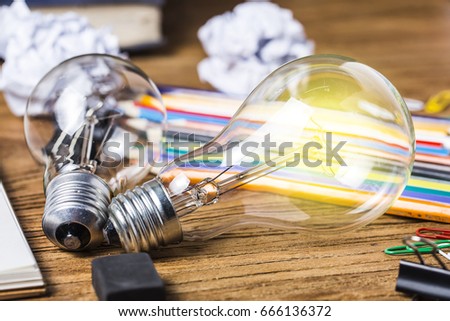 Glowing white light bulb with many pencils and notebook on wood table, creative writing concept