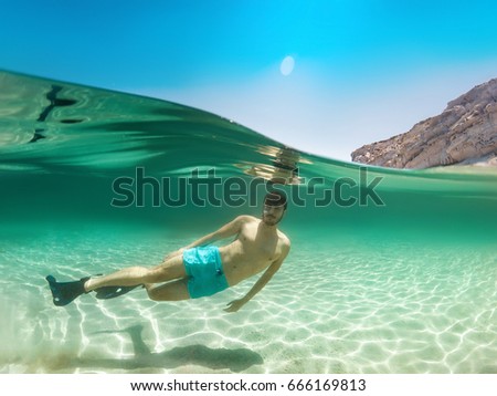 Split of above and half underwater photo of young guy swimming in sea